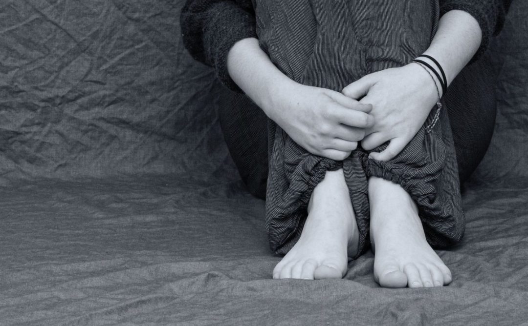 black and white photo of a person sitting with their hand around their legs