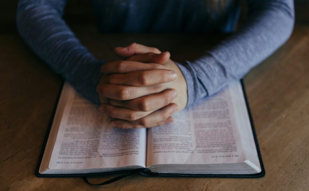 This is a picture of a persons hands folded in prayer laying on an open Bible. Observing Lent is about focusing more on your relationship with God.