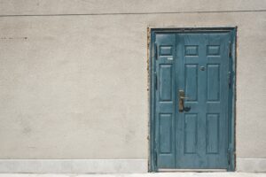 This is a picture of a teal door within a cream-colored wall.