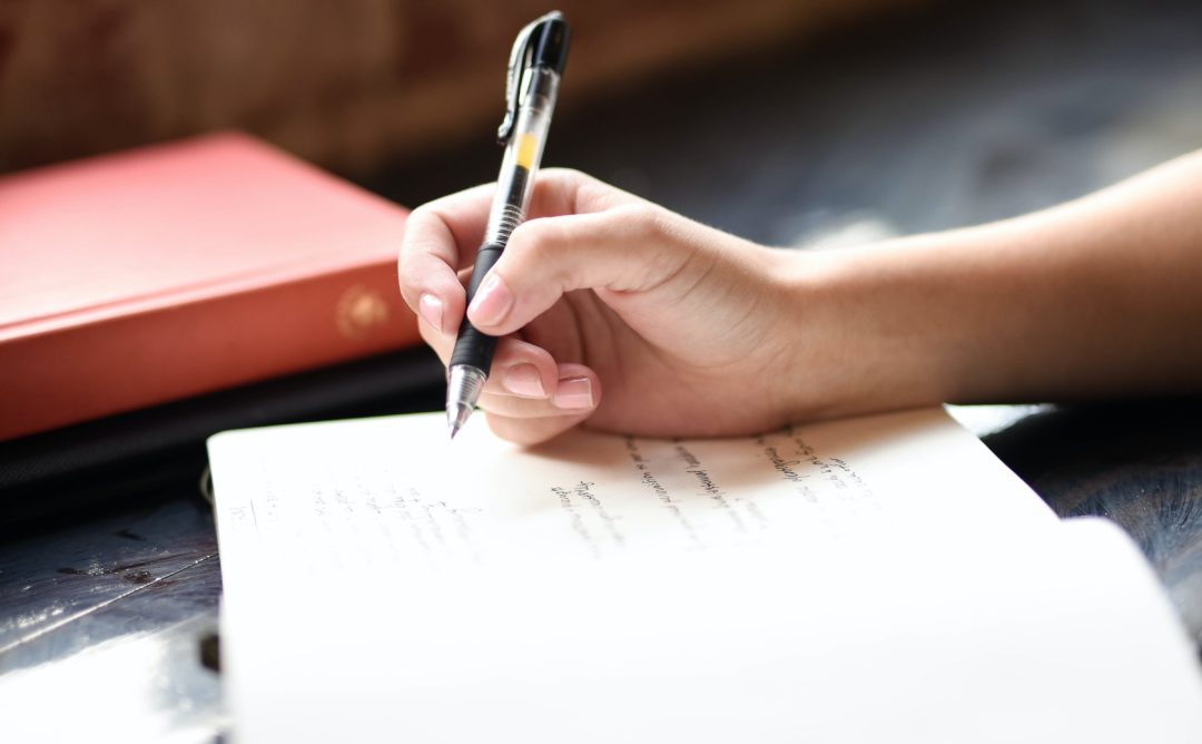 person writing in a journal by a sunny window