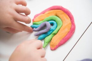 This is a picture a small pair of hands making a rainbow out of play-doh. This is a great sensory item to include in a mental health toolbox.
