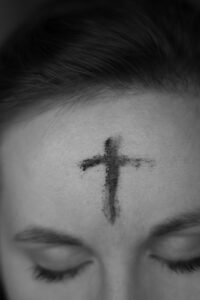 This is a picture of a woman with a cross made of ashes on her forehead. The picture is close up, only showing her eyes and up. You receive this cross on Ash Wednesday, the first day of Lent.