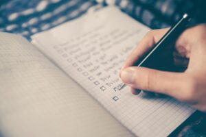 This is a picture of a to-do list in an open notebook. There is a hand holding a black pen about to add to the list. As I transition from summer, I adjust my routines.