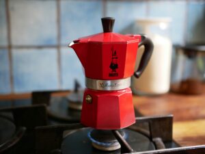 This is a photo of a red metal coffee percolator sitting on a stove eye. You can tell that the stove is on, because the eye has a blue ring. The smell of coffee brewing is a small thing that I celebrated.