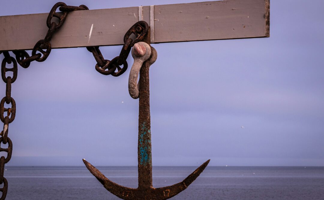 This is a picture of a brown metal anchor connected a a chain. It is handing from a wooden board. It represents God, who is our anchor in the waves.