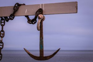 This is a picture of a brown metal anchor connected a a chain. It is handing from a wooden board. It represents God, who is our anchor in the waves.