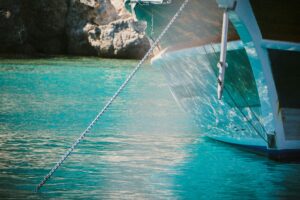 This is a picture of part of a brown and white boat in a bright blue body of water. There is a rope coming from the boat and going into the water. This is likely the rope connecting the boat to the anchor.